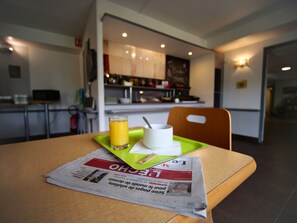 A breakfast setup with a newspaper, a glass of orange juice, and a white cup on a green tray.