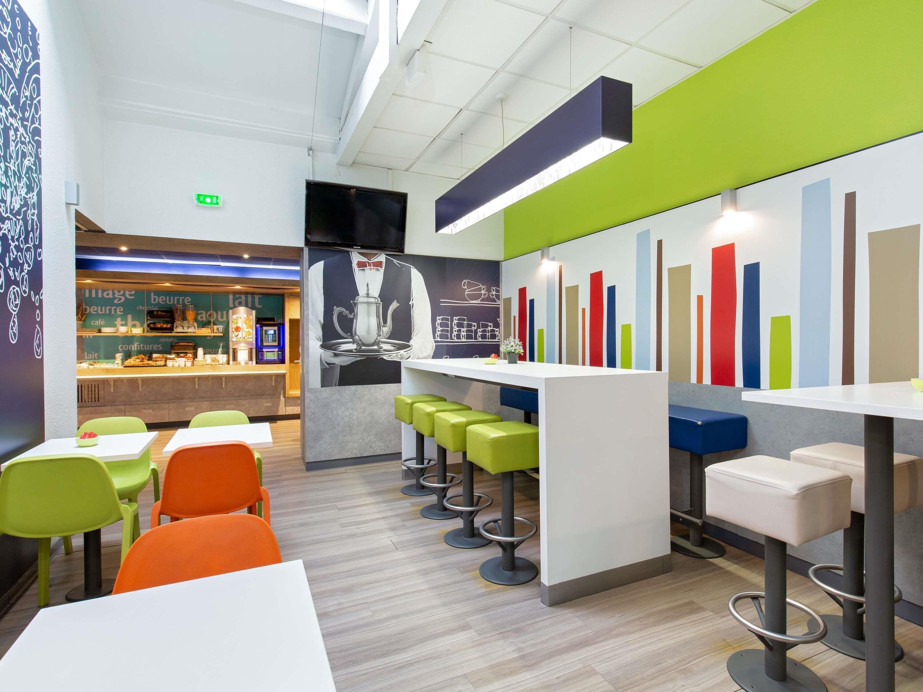 A modern café interior with a bar area, seating with stools, and a colorful bar chart on the wall.