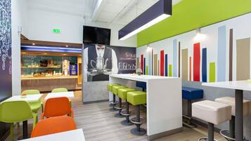 A modern café interior with a bar area, seating with stools, and a colorful bar chart on the wall.