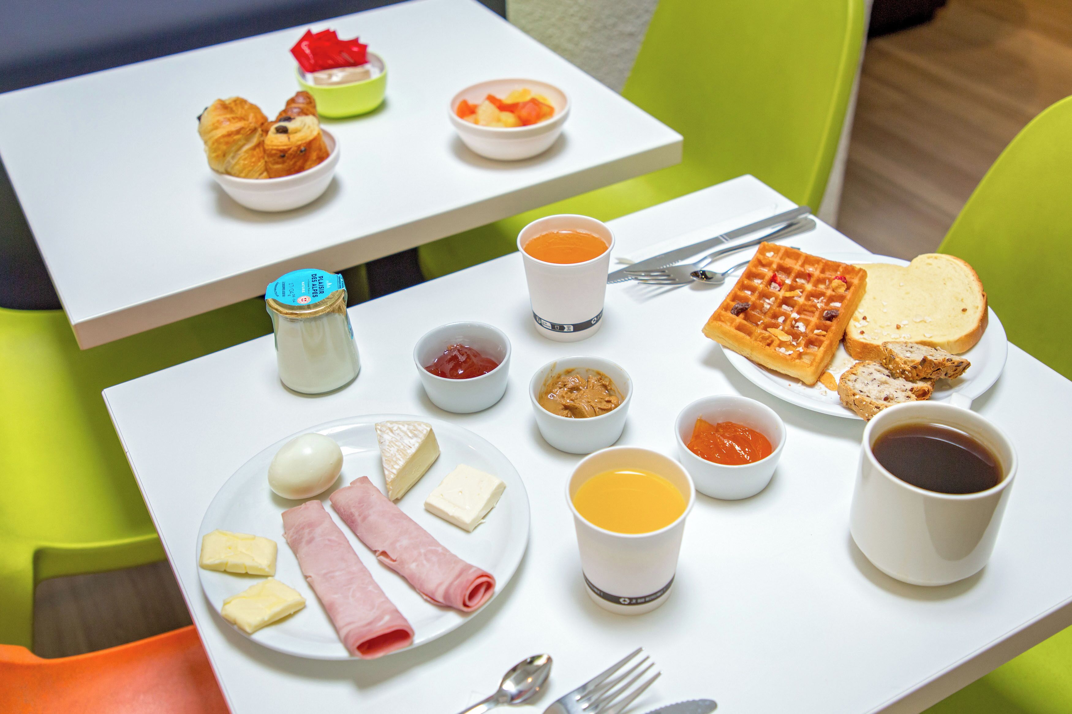 A breakfast table with croissants, fruit, waffles, toast, cheese, ham, butter, jam, and coffee.