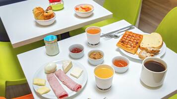A breakfast table with croissants, fruit, waffles, toast, cheese, ham, butter, jam, and coffee.