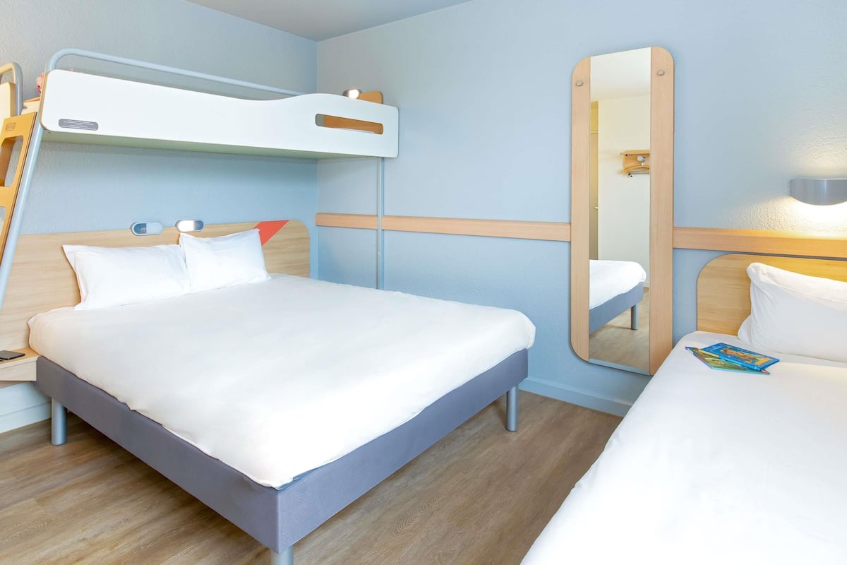 Una habitación de hotel moderna con una cama litera, una mesita de noche, un espejo y una lámpara de noche.