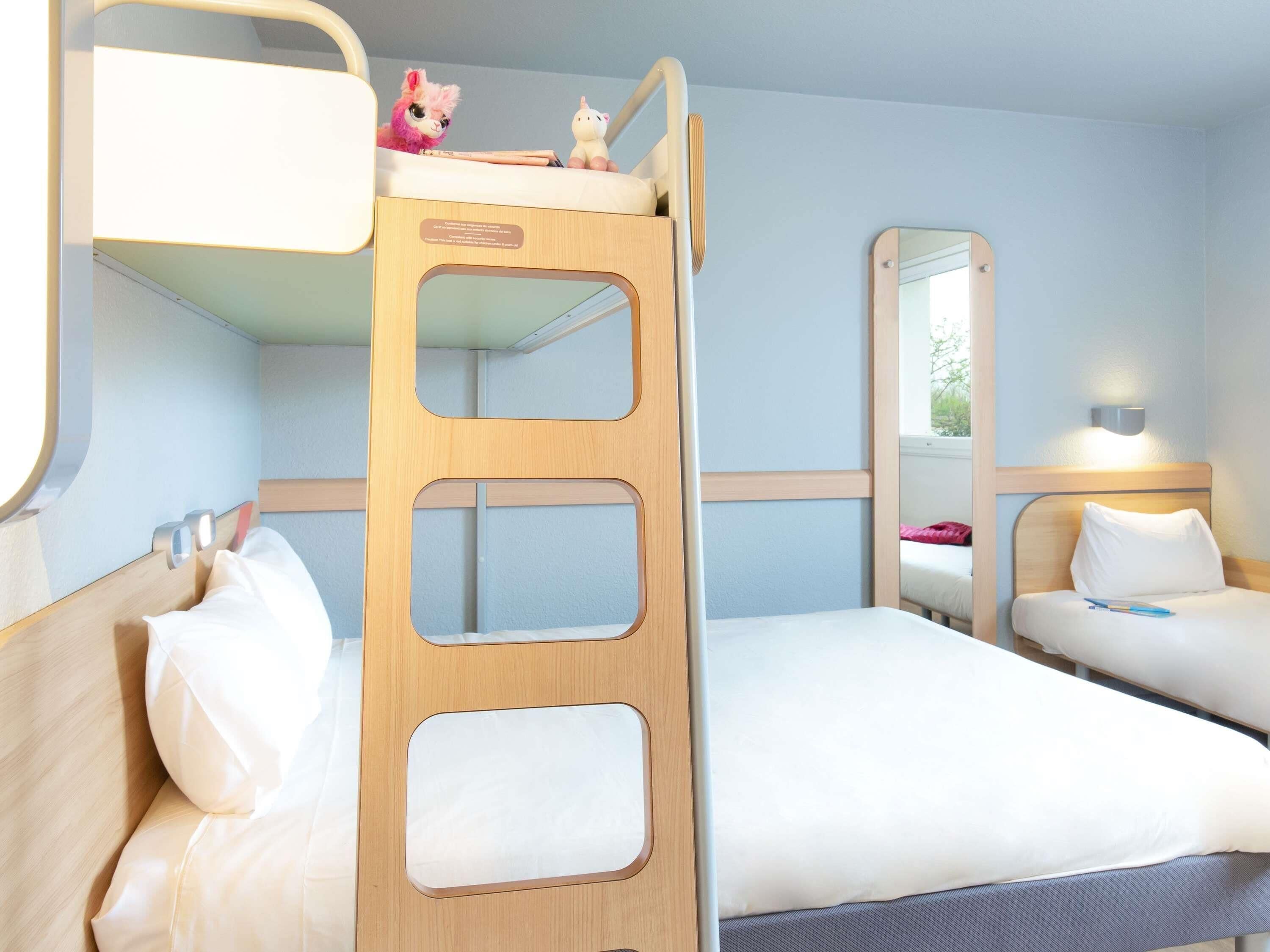 A bunk bed room with a wooden ladder, a mirror, and a small desk with toys.
