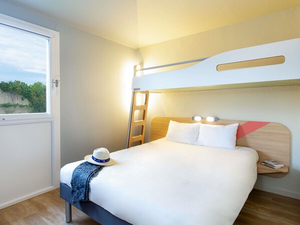 Habitación de hotel con literas, ventana con vistas, mesita de noche con lámpara y un sombrero sobre la cama.