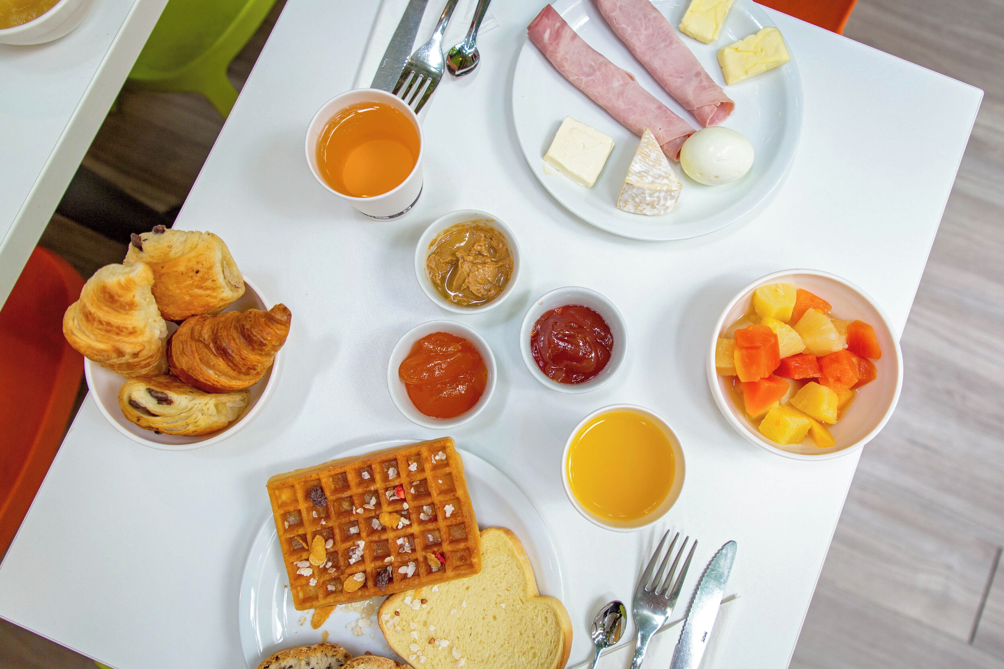 A breakfast plate with croissants, waffles, cheese, ham, eggs, and fruit.