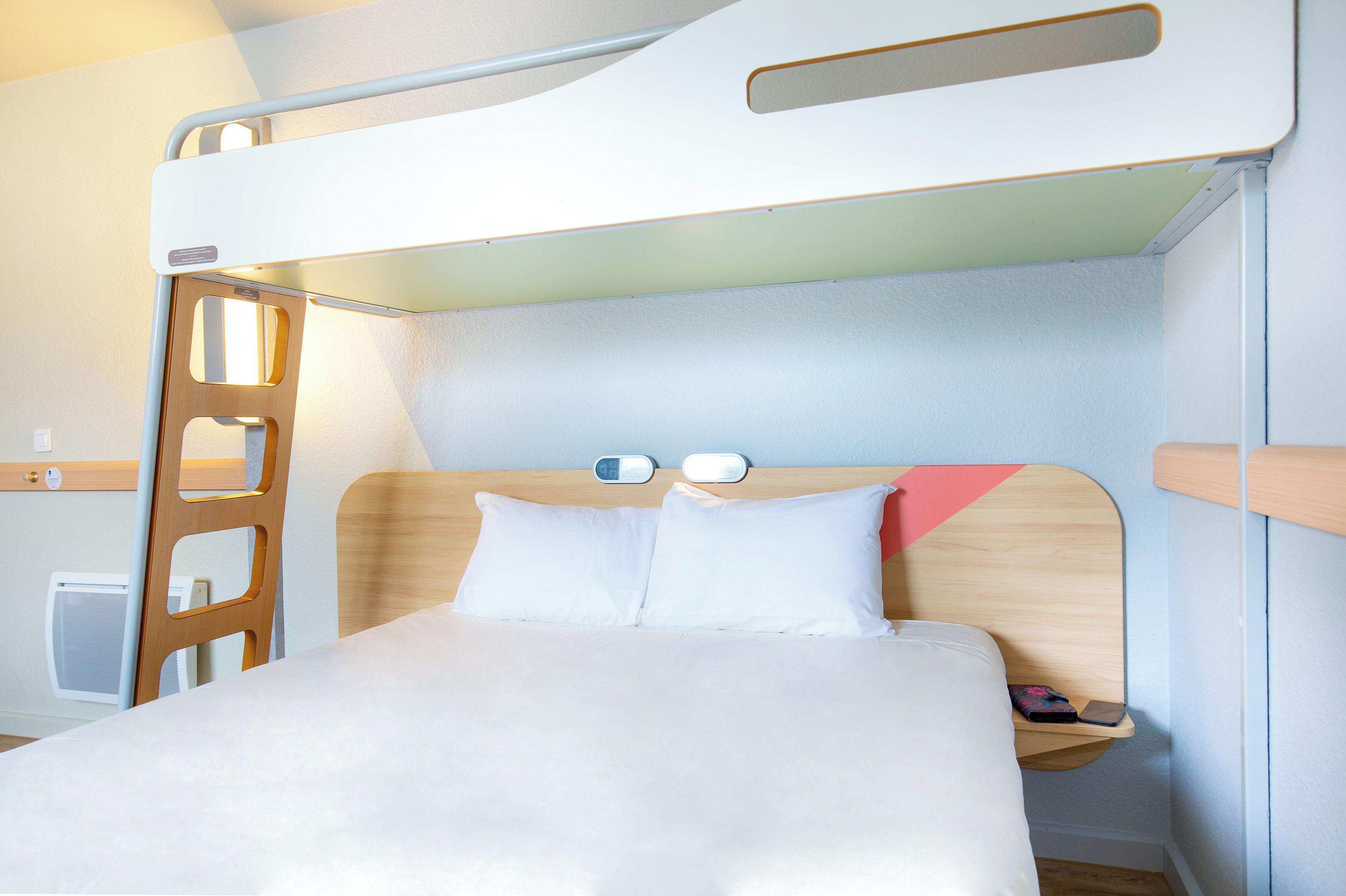 A bunk bed with a wooden headboard, white bedding, and a small bedside table with a lamp.