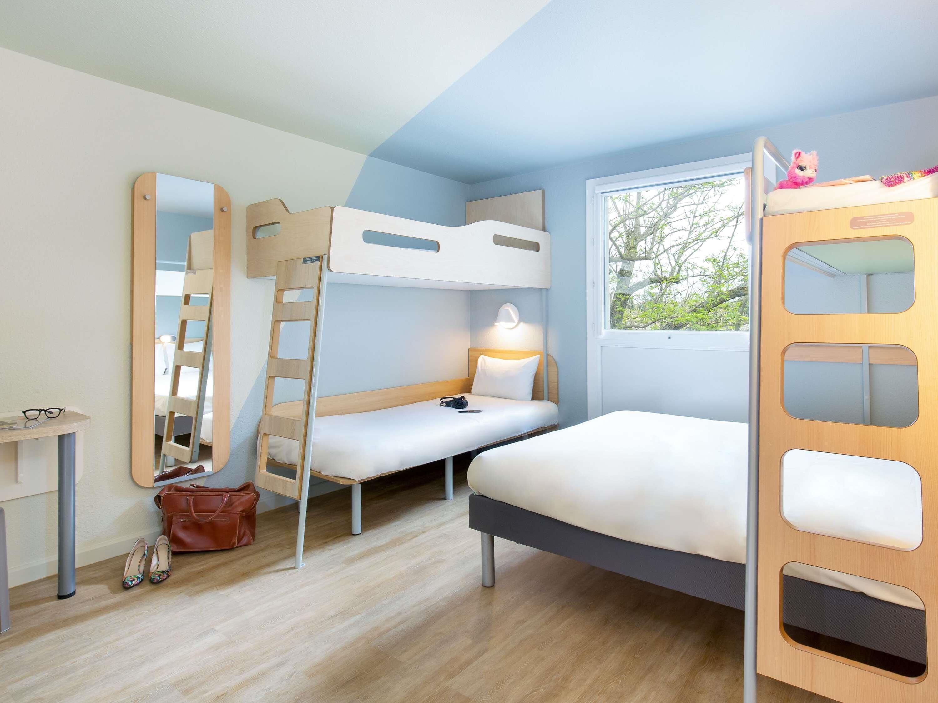 A bunk bed room with a desk, ladder, and a window with a view.