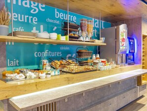 A café counter with shelves displaying bread, pastries, and breakfast items. - ibis budget Cavaillon (Cavaillon)