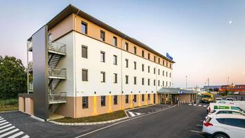 Een modern hotel met een plat dak, veel ramen en een parkeerplaats met auto's.
