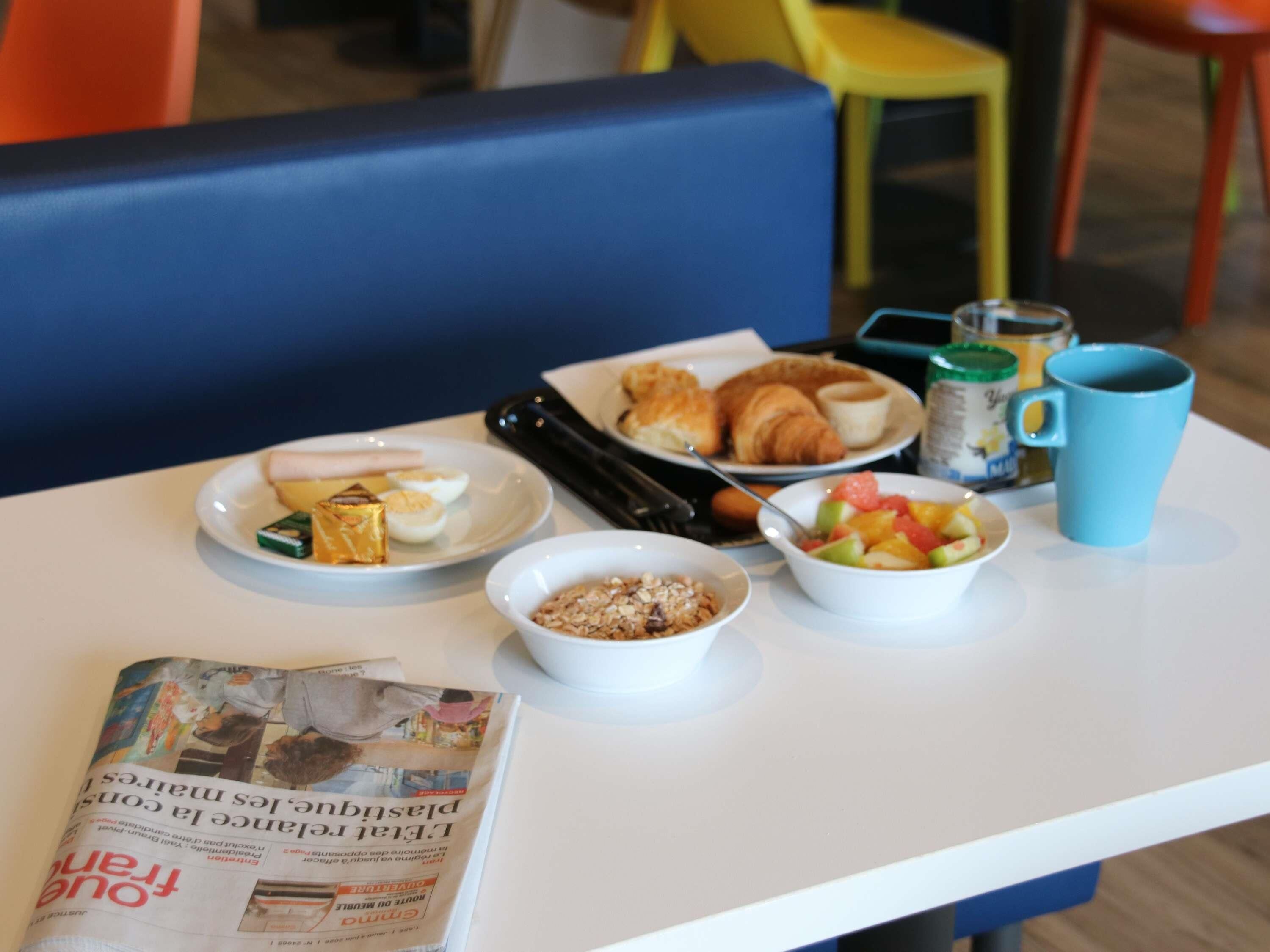 A breakfast table with plates of food, a coffee mug, a newspaper, and a magazine.