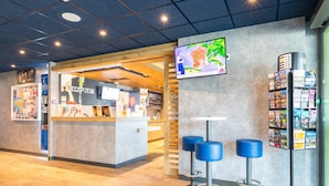 A reception area with a counter, a TV mounted on the wall, and a magazine rack. - ibis budget Rennes Route de Lorient (Rennes)