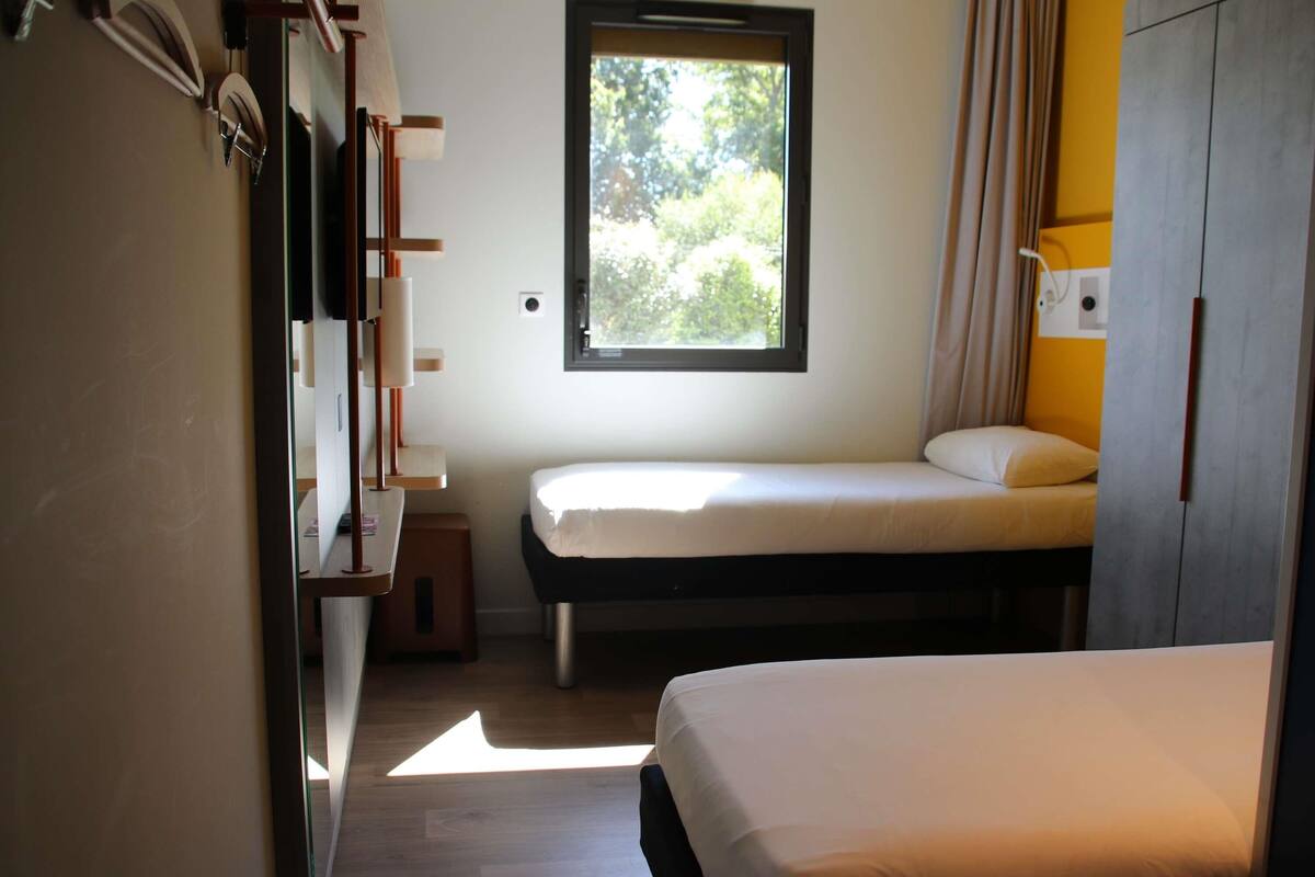 Une chambre avec deux lits, une fenêtre et une armoire.