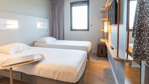 A hotel room with two beds, a desk with a laptop, a TV, and a window with curtains. - ibis budget Rennes Route de Lorient (Rennes)