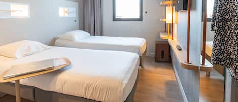 A hotel room with two beds, a desk with a laptop, a TV, and a window with curtains.