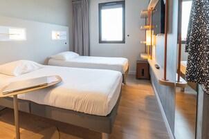 Une chambre d’hôtel avec deux lits, un bureau avec un ordinateur portable, une télévision et une fenêtre avec des rideaux.