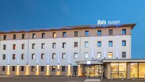 A modern hotel building with multiple floors, a covered entrance, and illuminated windows. - ibis budget Rennes Route de Lorient (Rennes)