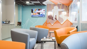 Ein stilvoller Lounge-Bereich mit Sitzgelegenheiten, einem kleinen Tisch mit einer Zeitschrift und einem an der Wand montierten Fernseher.
