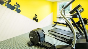 Ein Fitnessraum mit Laufband, Ergometer und einer Wand mit Silhouetten von Radfahrern.