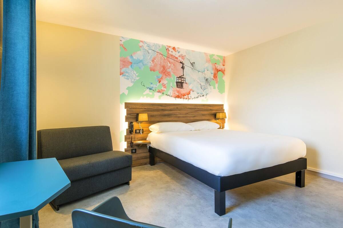 A hotel room with a bed, a sofa, a desk, and a wall map.