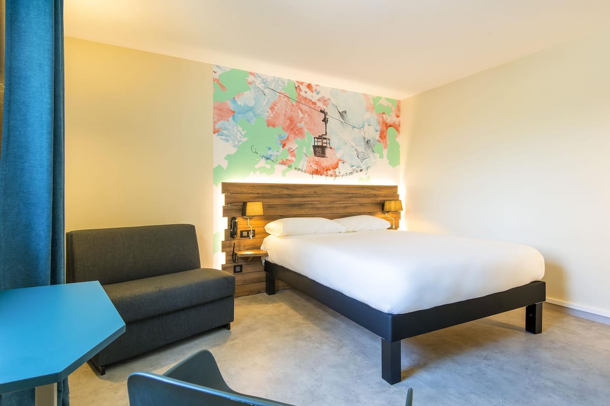 A hotel room with a bed, a sofa, a desk, and a wall map.