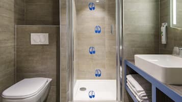 A modern bathroom with a glass-enclosed shower, a toilet, and a sink with a towel rack.
