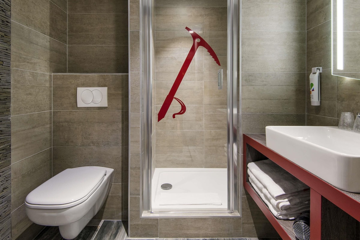 A modern bathroom with a glass-enclosed shower, a white toilet, and a red towel rack.