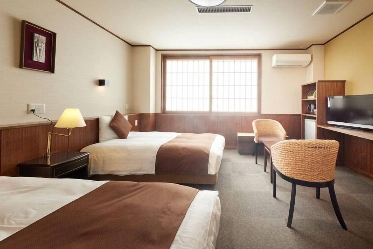 Habitación de hotel con dos camas, televisión, una silla y ventana.