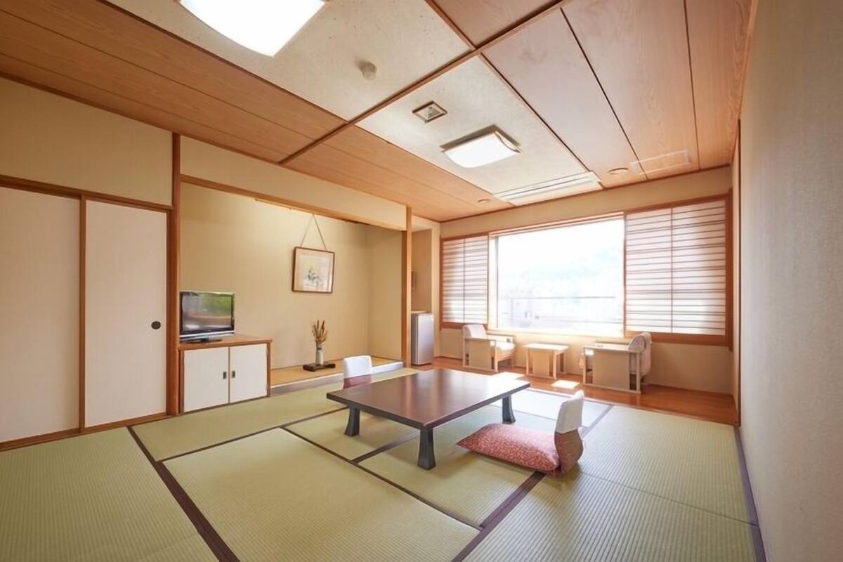 Una habitación japonesa tradicional con suelo de tatami, una mesa baja, puertas correderas y un ventanal grande.