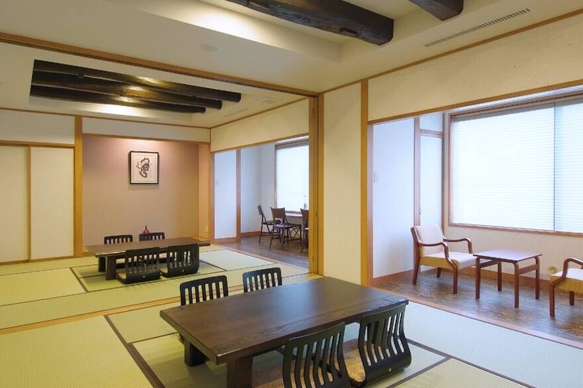 Ein traditioneller japanischer Raum mit Tatami-Bodenbelag, einem Holztisch, Stühlen und großen Fenstern.
