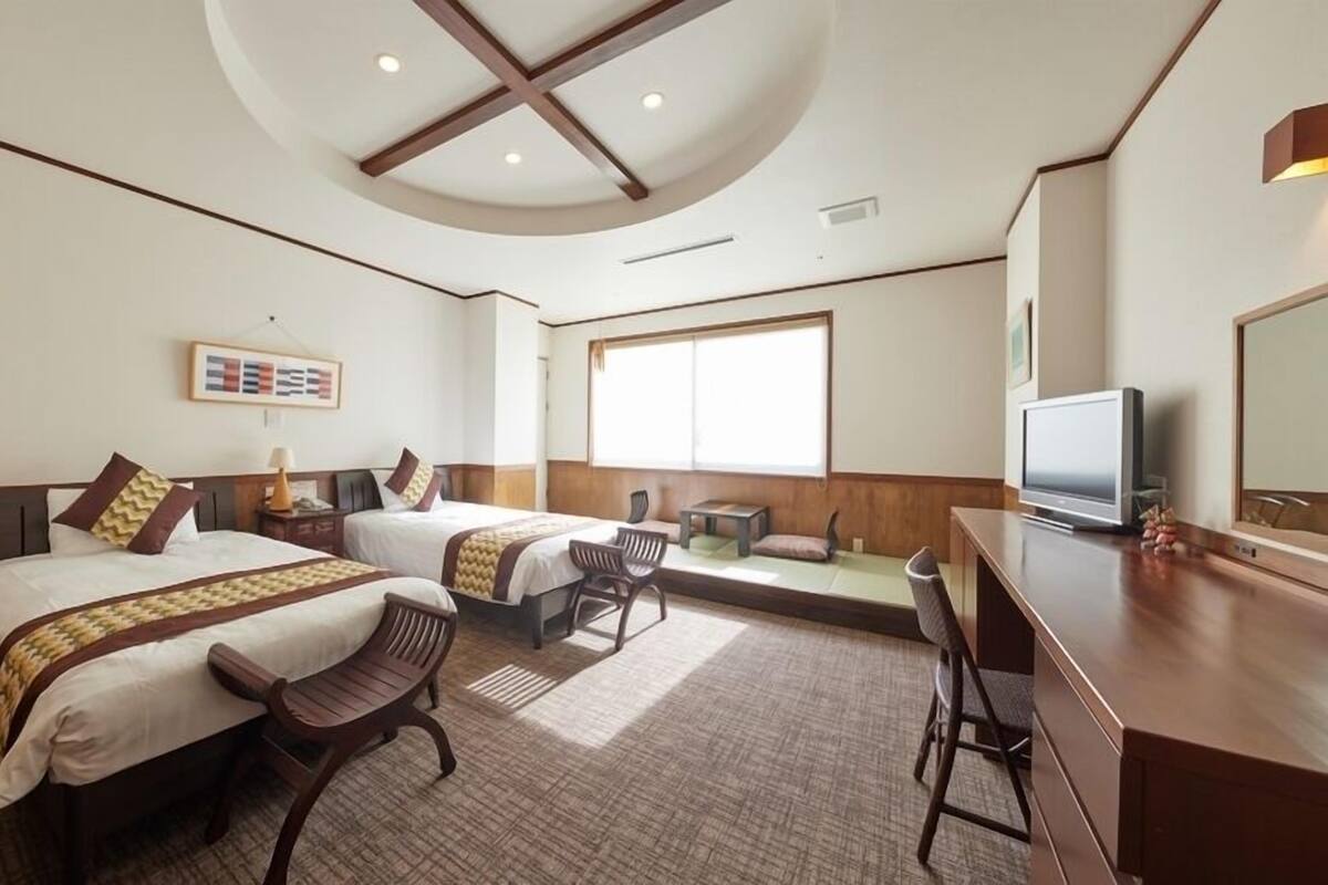 Habitación de hotel con dos camas, un escritorio, un televisor y un ventanal grande.