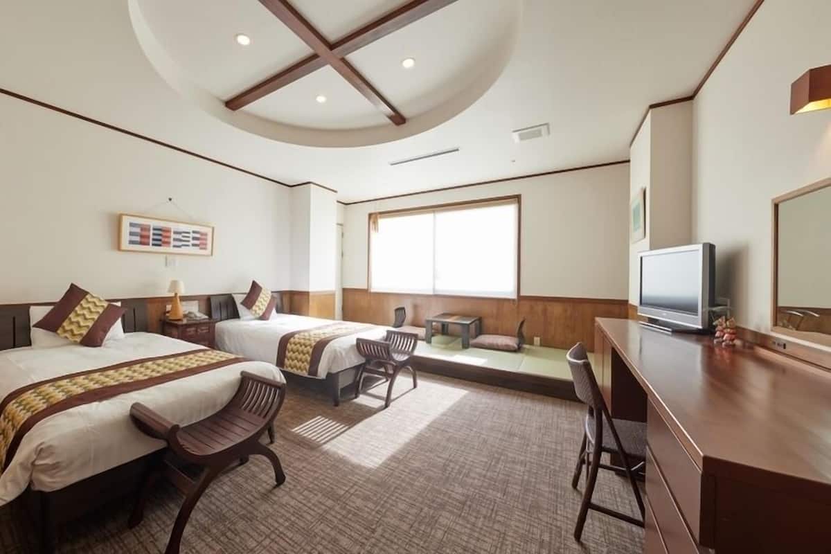 Habitación de hotel con dos camas, un escritorio, un televisor y un ventanal grande.