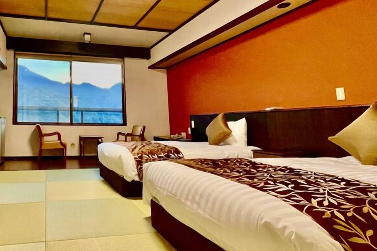Habitación de hotel con dos camas, un ventanal con vistas a la montaña, una mesita y una silla.