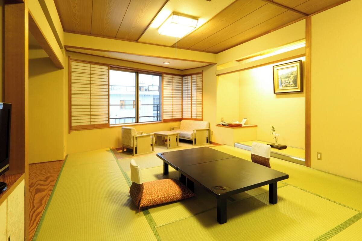 Una habitación con tatami, una mesa baja, un sofá y un televisor.