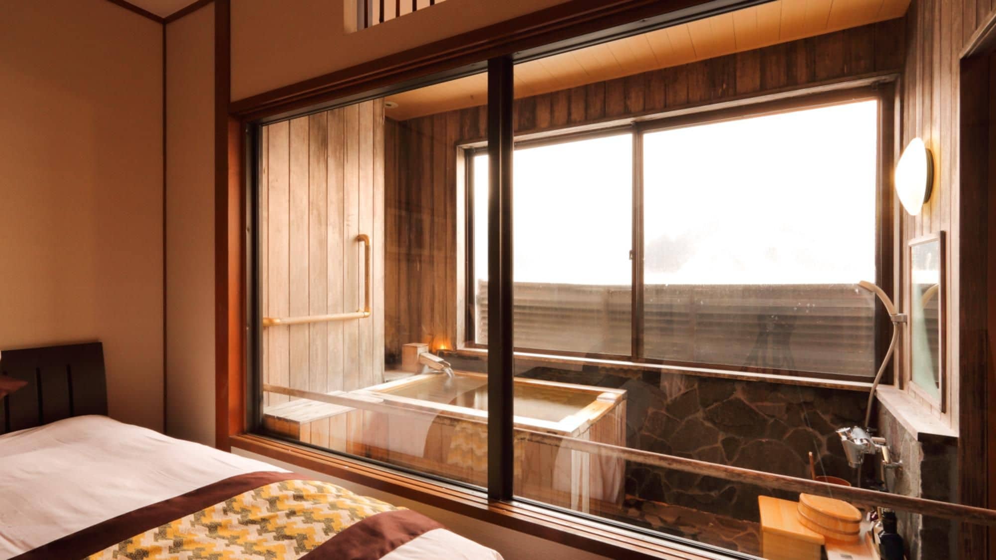 A room with a large window, a bed, a wooden wall, and a stone wall.