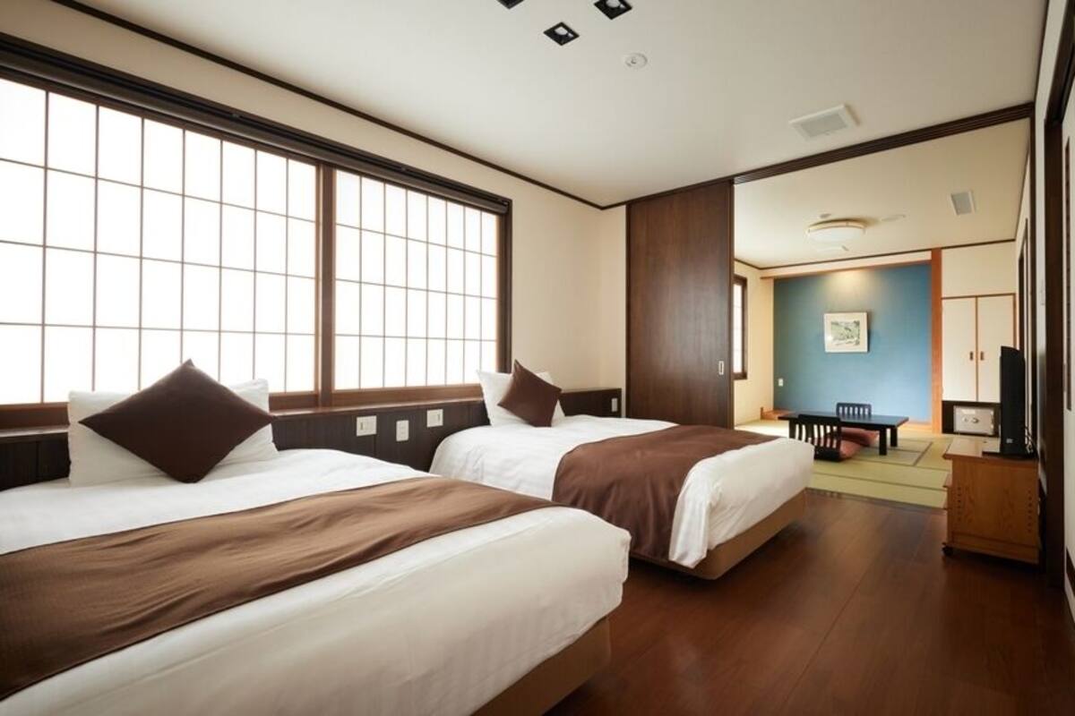 Habitación de hotel con dos camas, zona de comedor y vista a la ciudad.