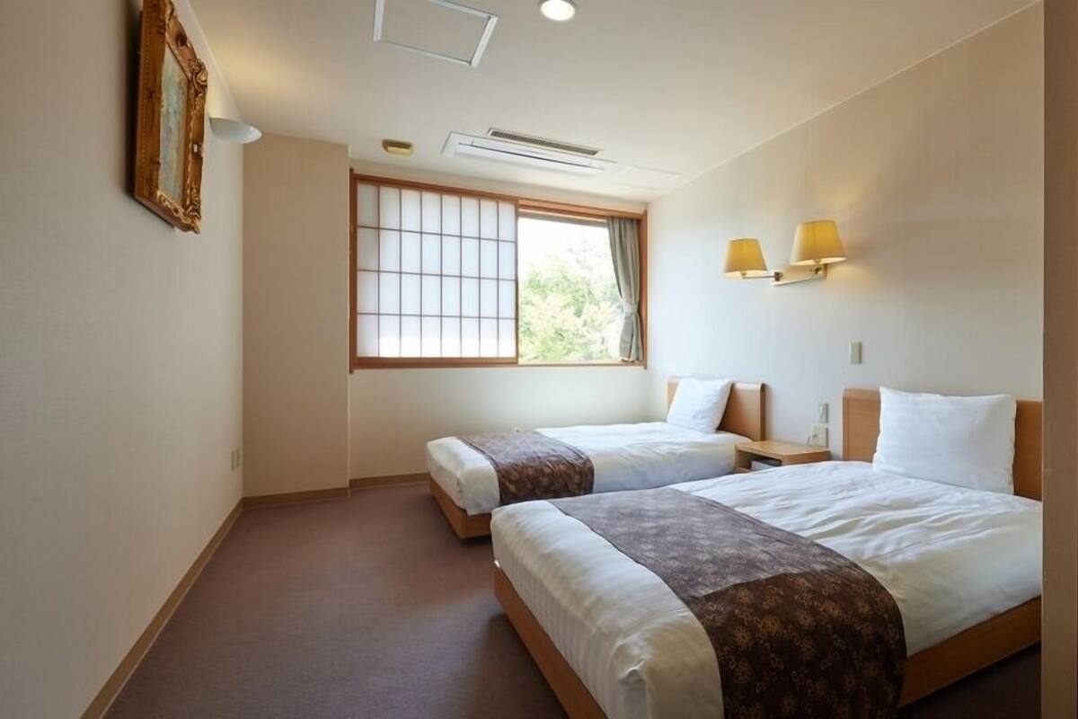 Una habitación de hotel con dos camas, una ventana con vistas, un aire acondicionado y una lámpara fijada a la pared.