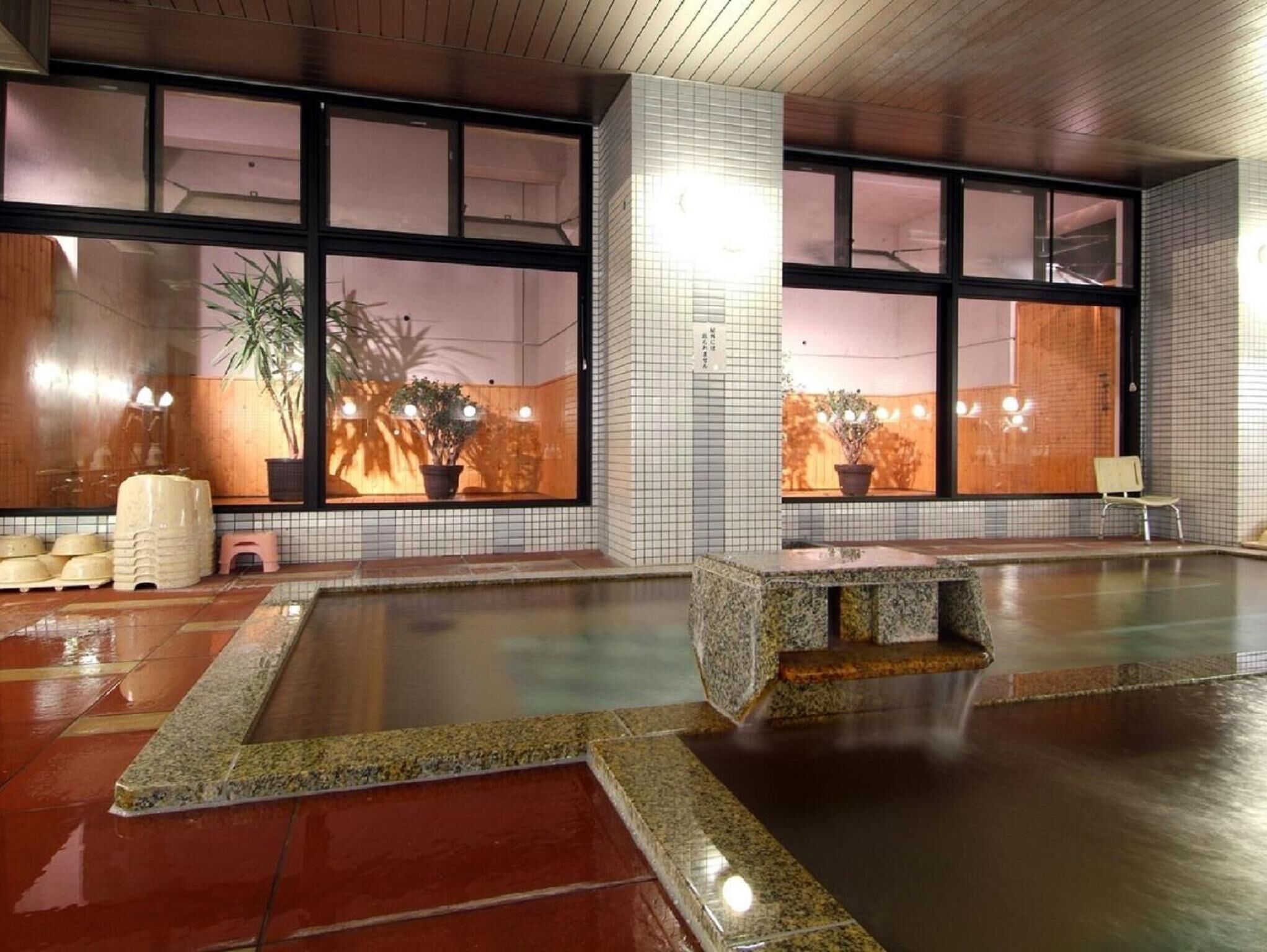 A large indoor pool with a stone bench, tiled walls, and potted plants.