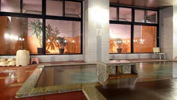 A large indoor pool with a stone bench, tiled walls, and potted plants.