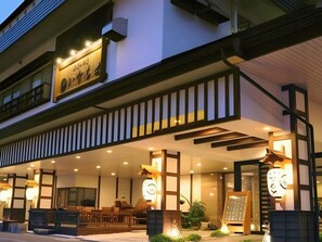 A hotel with a covered outdoor seating area, a signboard, and a staircase leading to the entrance. - Inamoto (Yuzawa)