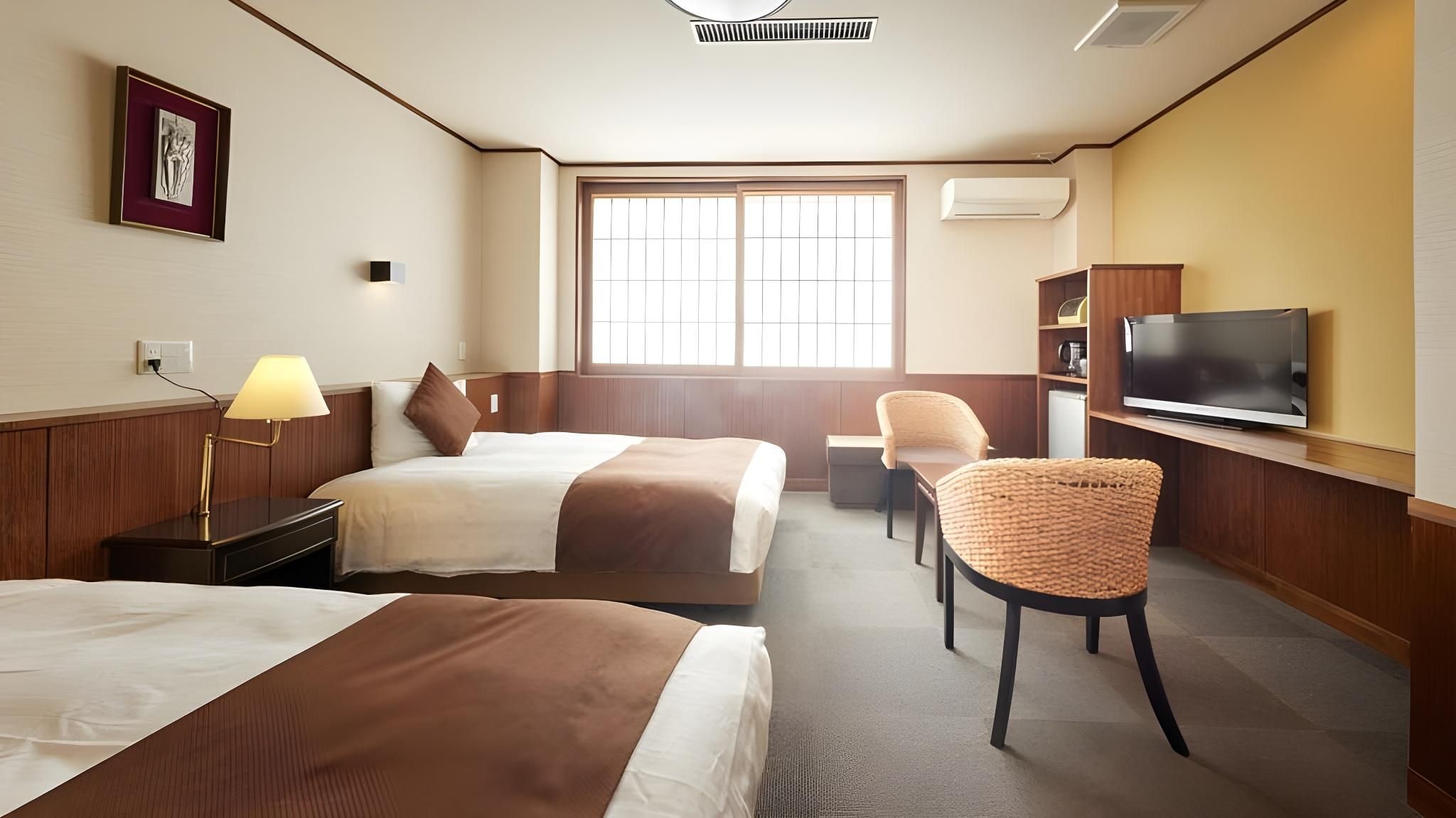 Een hotelkamer met twee bedden, een bureau, een stoel, een televisie en een raam.