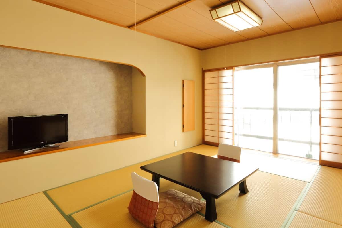 Una habitación japonesa tradicional con suelo de tatami, una mesa baja, un televisor y puertas correderas.