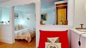 Quarto com cama, uma cadeira vermelha, um espelho e janela com vista para um prédio.