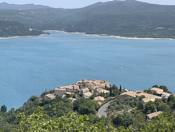 A coastal town with buildings surrounded by greenery and a clear view of the sea.