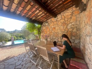A covered outdoor seating area with a stone wall, a wooden table, and chairs. - Private country house, garden, and relaxation between the sea and lake (Draguignan)