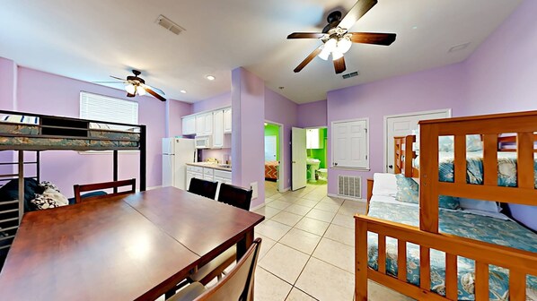 A compact apartment with a dining area, kitchen, and a bedroom with bunk beds.
