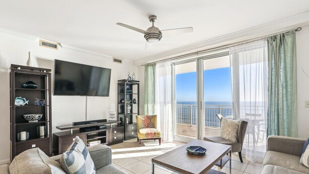 En moderne stue med et fladskærms-tv, en loftventilator og en balkon med havudsigt.