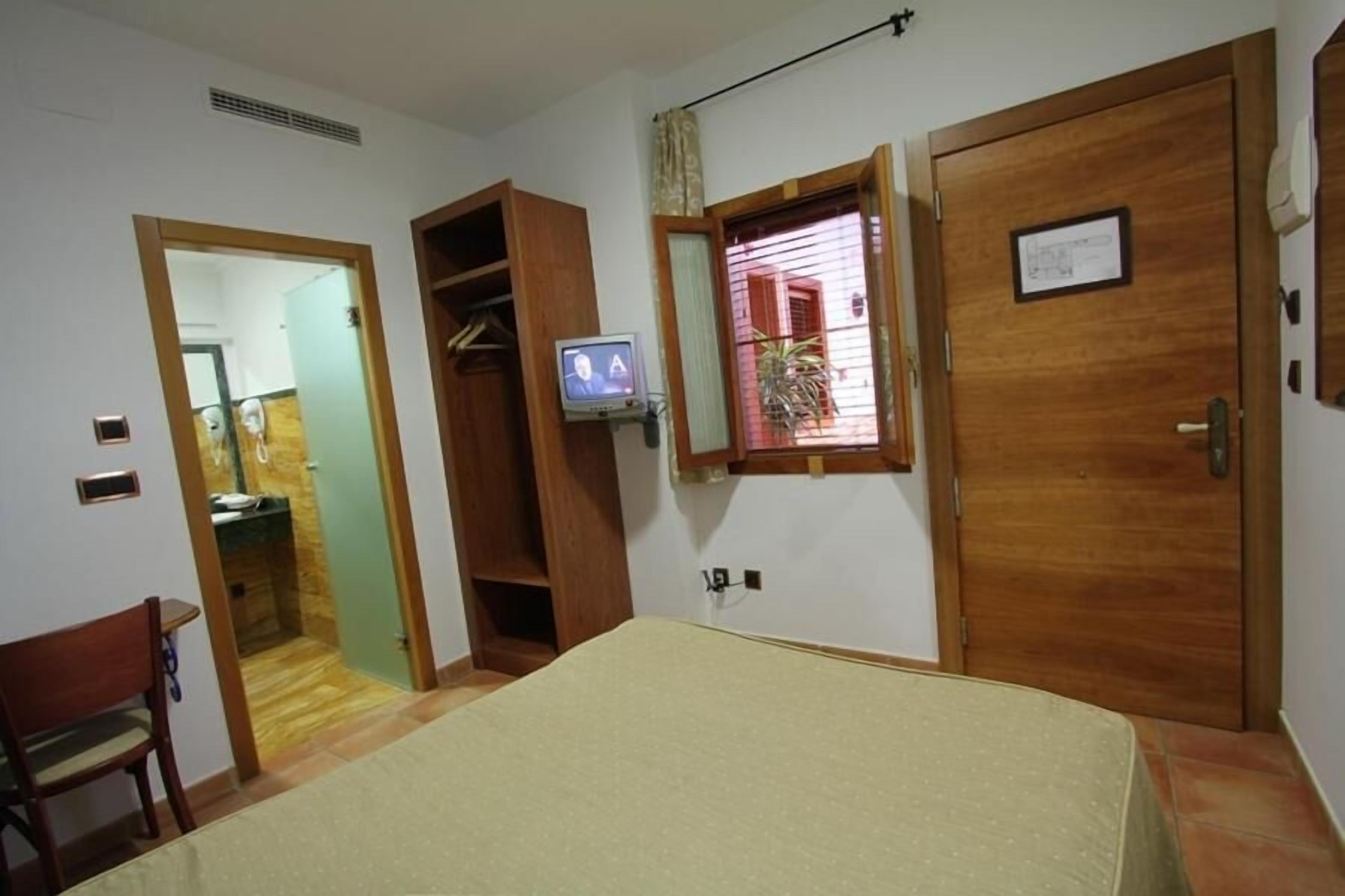 Un dormitorio con cama, televisor, armario de madera y ventana con persianas.
