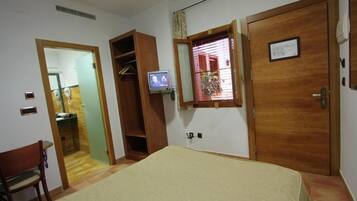 Un dormitorio con cama, televisor, armario de madera y ventana con persianas.