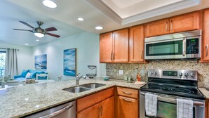 A modern kitchen with granite countertops, stainless steel appliances, wooden cabinets, and a ceiling fan. - LAKE PALMS 7 - Newly Updated Sanibel Condo Overlooking Lagoon (Sanibel)