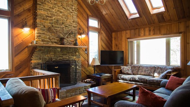 A cozy log cabin interior with a stone fireplace, wooden furniture, and a television. - Riverfront - main level master bedroom - now with high speed unlimited Internet! (Bowden)